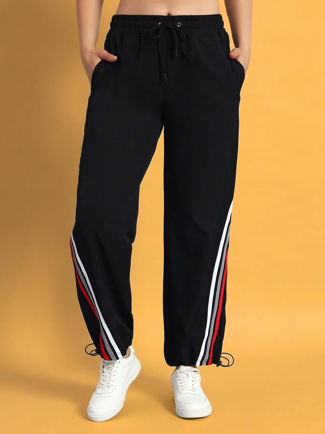 Woman wearing black relaxed fit jogger pants with stripe detail, paired with white sneakers.