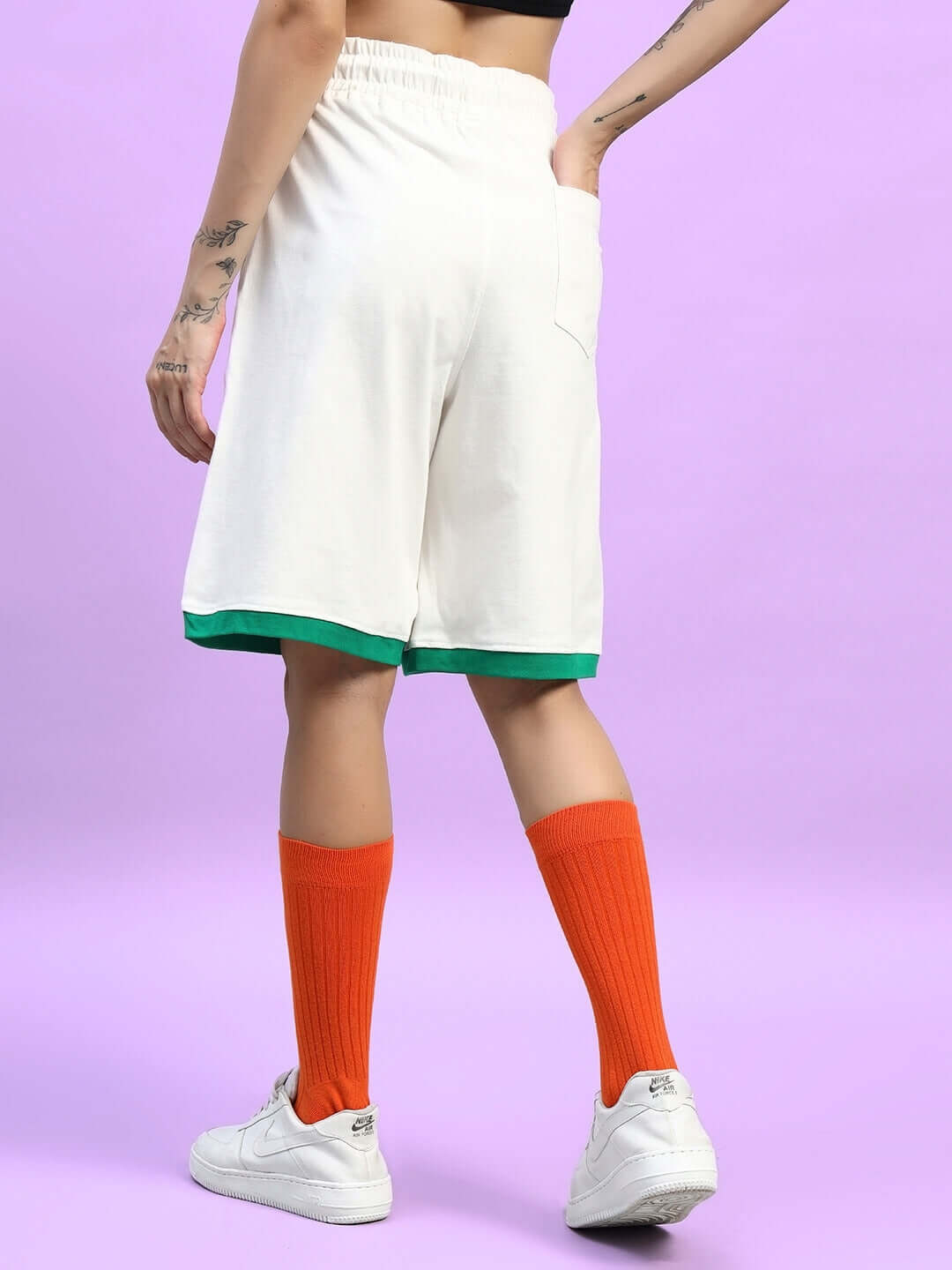 Back view of WOMEN'S DRIBBLE CO-ORD SET OFF WHITE shorts with orange socks and white sneakers against purple background.