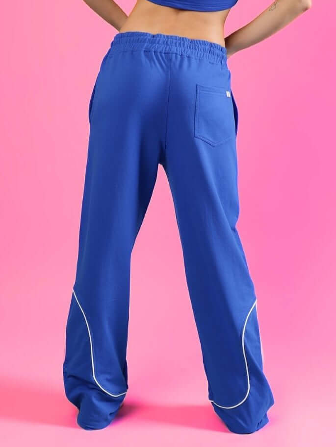 Women's blue joggers with contrast piping detail, back view, on a bright pink background, showcasing comfortable fit and casual style.