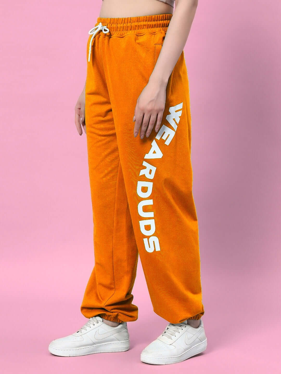 Woman wearing WOMEN'S ELLEN RELAXED FIT JOGGER ORANGE against pink background.
