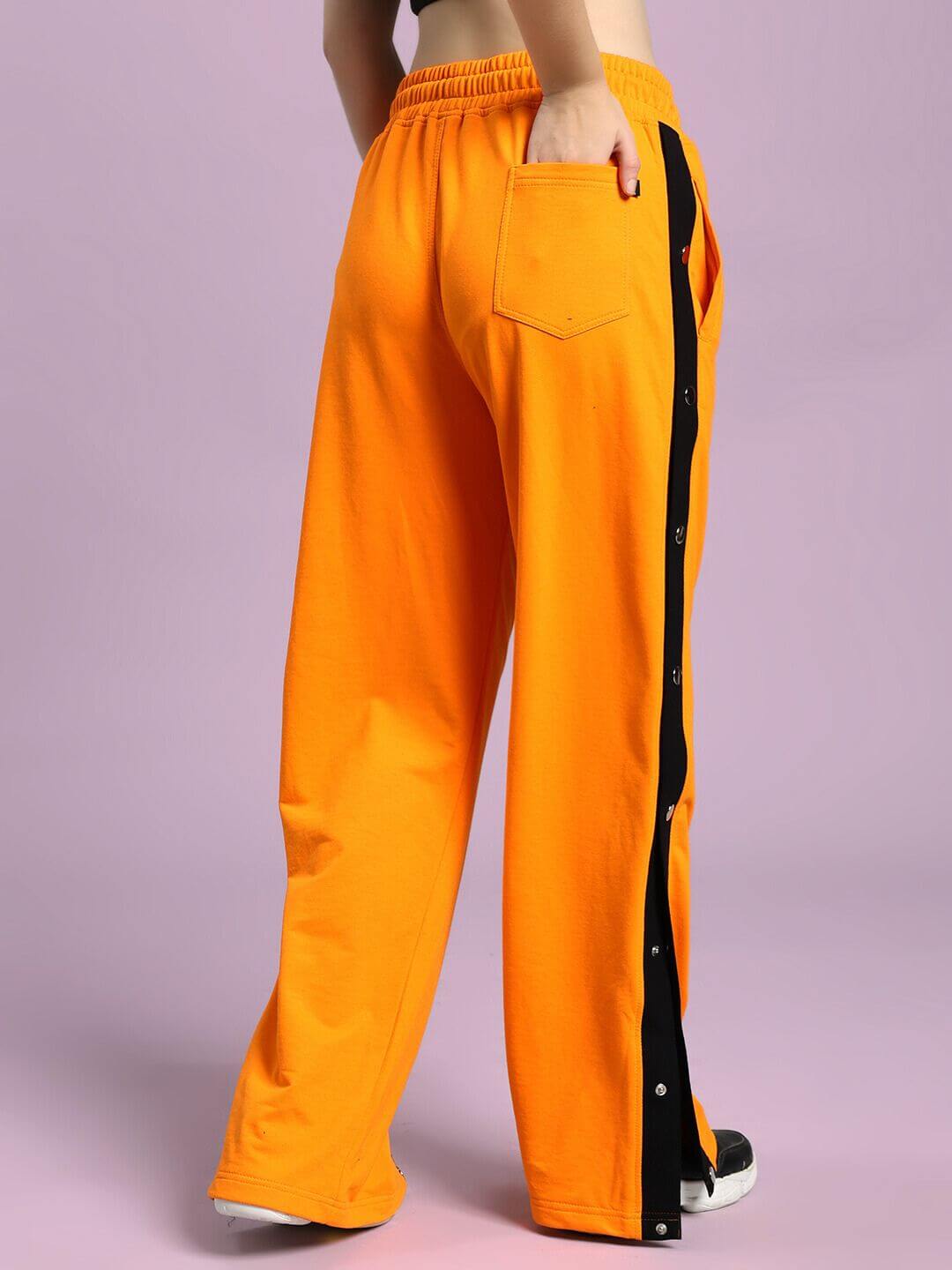 Rear view of WOMEN'S EMBER BOLT SIDE JOGGER ORANGE with bold side stripe on light purple background