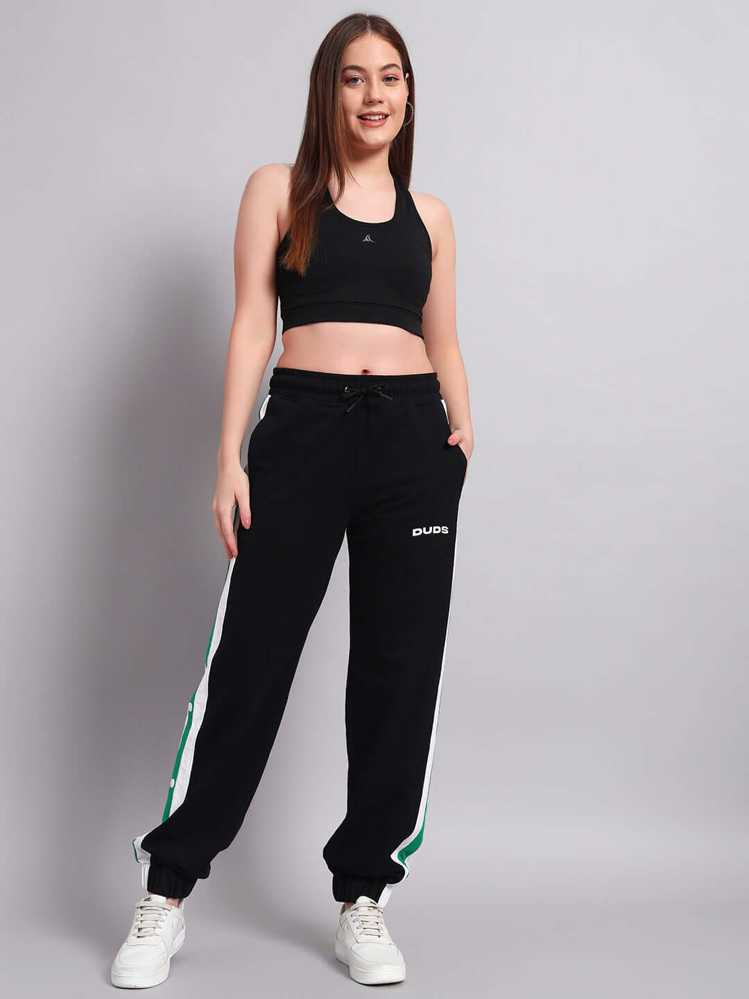 Woman wearing black-green Emirati stripes joggers by DUDS, standing confidently, highlighting athletic fashion.