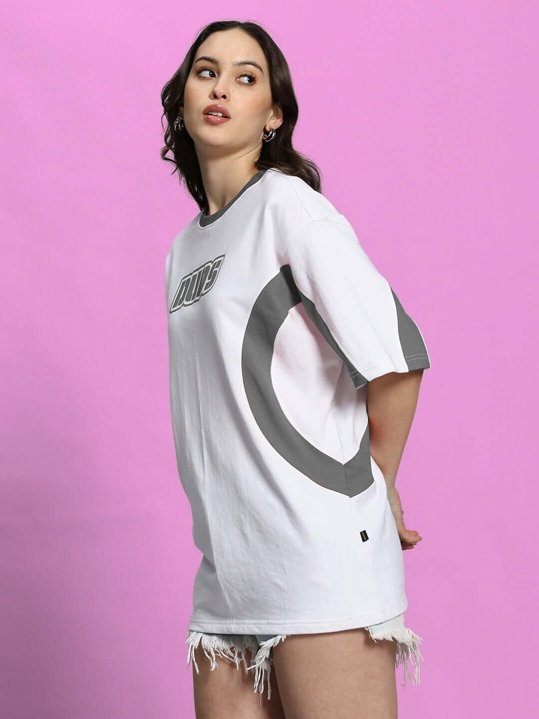 Model wearing women's oversized EZEL T-shirt in white grey, premium cotton blend, stylish design on pink background.