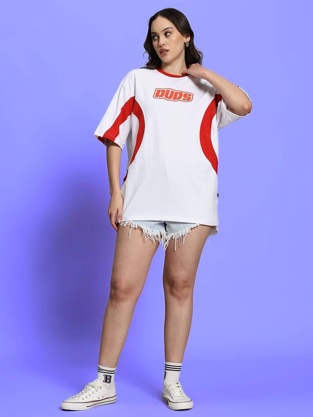 Model wearing oversized white-red women's t-shirt, DUDS logo, styled with denim shorts and sneakers. Casual, comfortable fashion look.