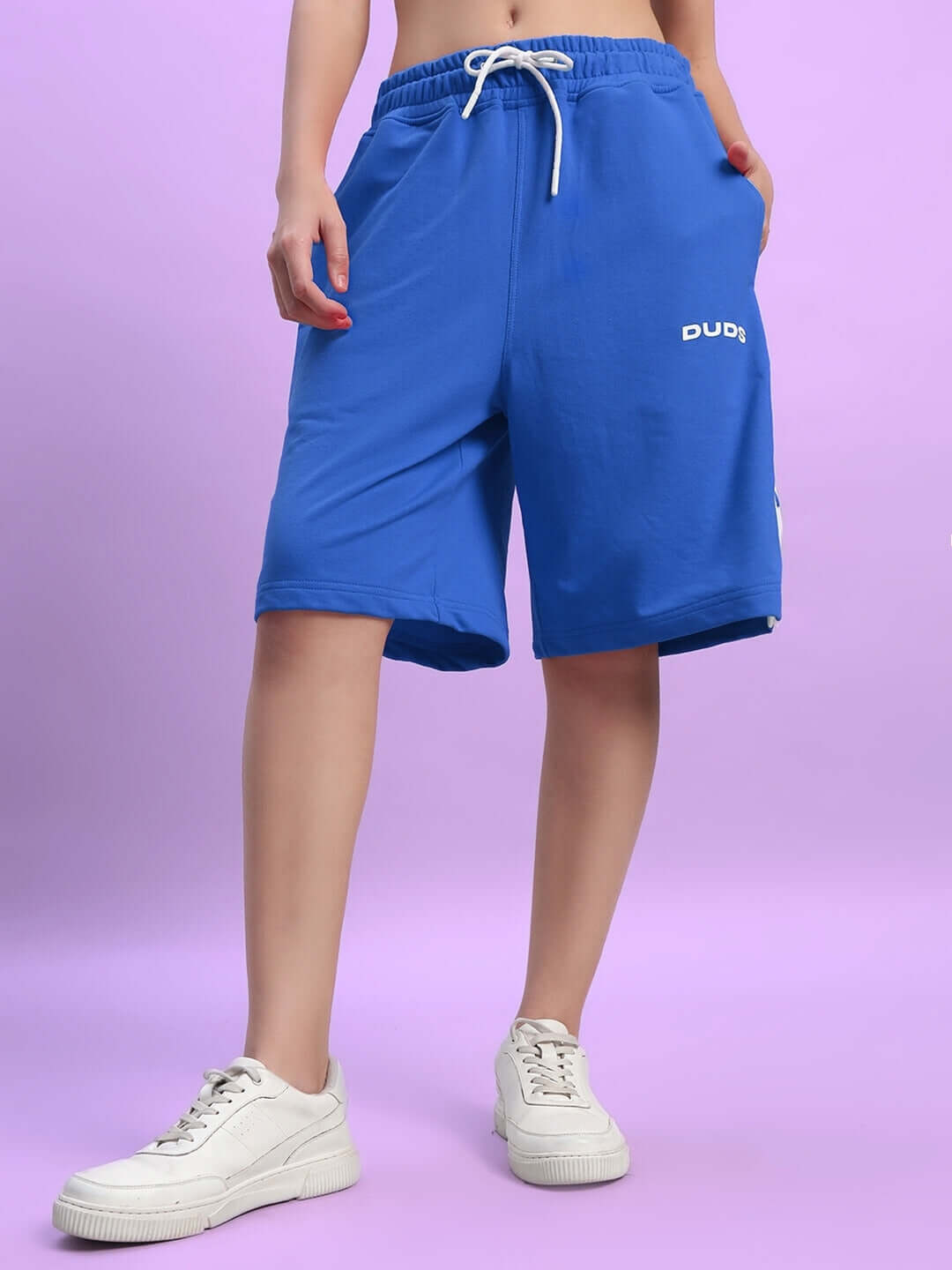 Model wearing blue women's Ezel regular fit shorts by DUDS, featuring custom fit option and comfortable design, paired with white sneakers.