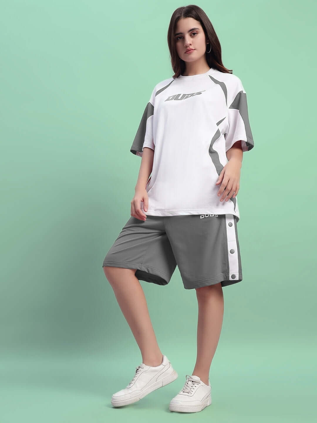 Woman wearing DUDS grey regular fit shorts and matching top, standing against a green background, showcasing comfortable casual wear.