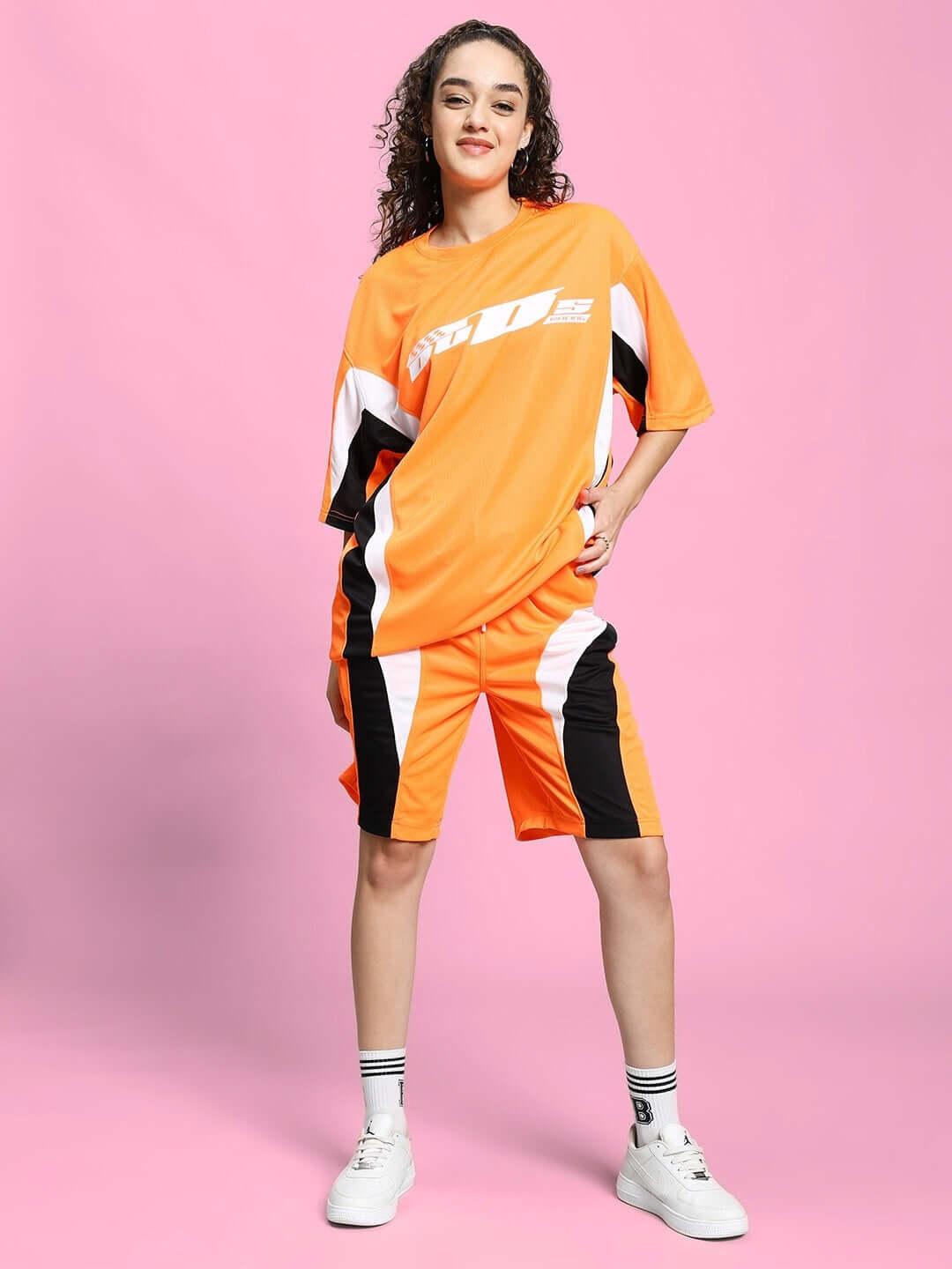 Woman wearing WOMEN'S FIFA COLORBLOCK CO-ORD SET ORANGE, featuring bold, sporty colorblock design on a pink background.
