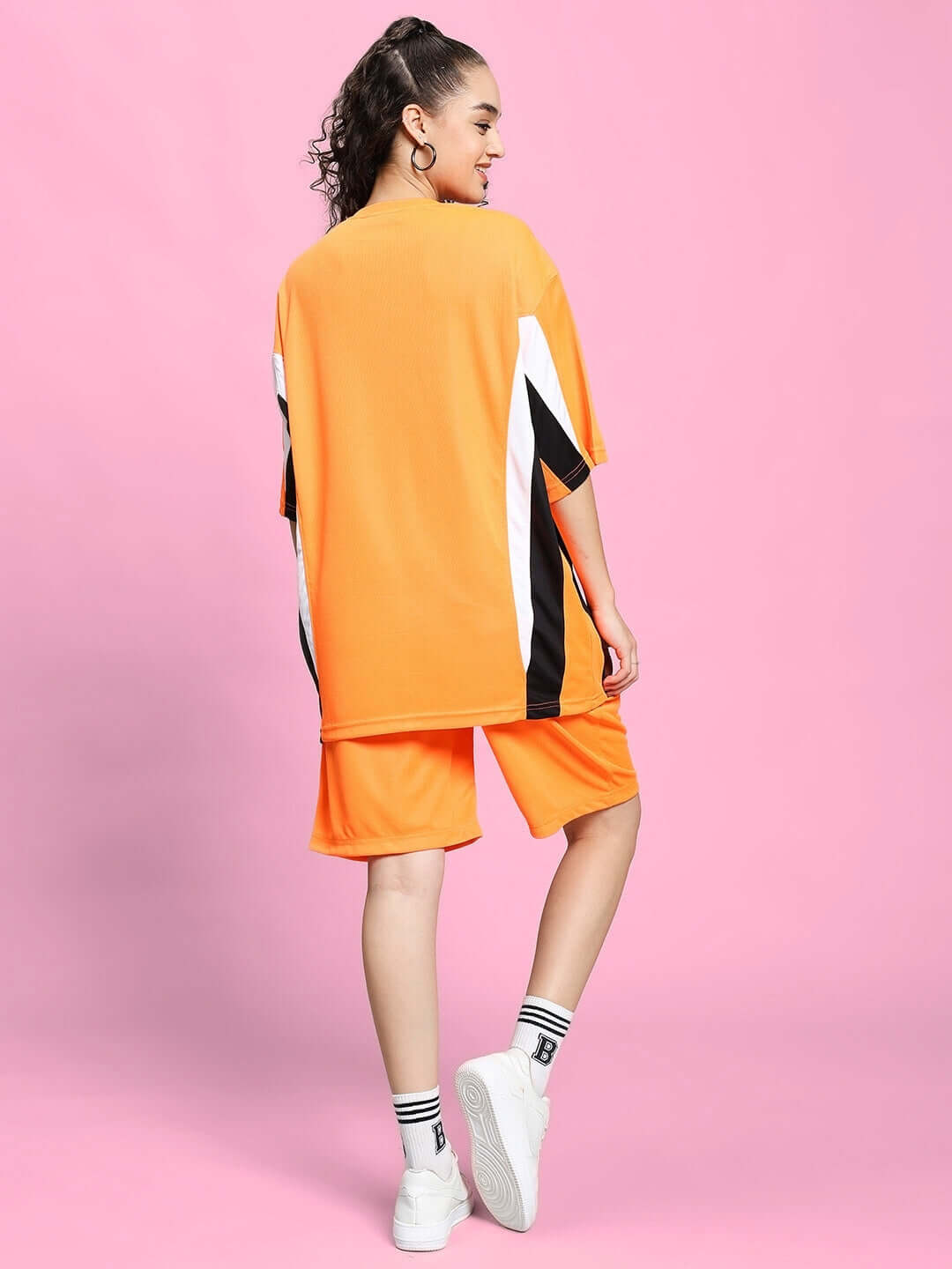 Model in WOMEN'S FIFA COLORBLOCK CO-ORD SET ORANGE with dynamic design in vibrant orange on pink background.