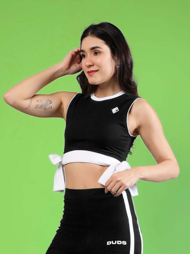 WOMENS FITTONIA COOL CROP TOP BLACK on a model with a green background, showcasing its stylish design and comfortable fit.