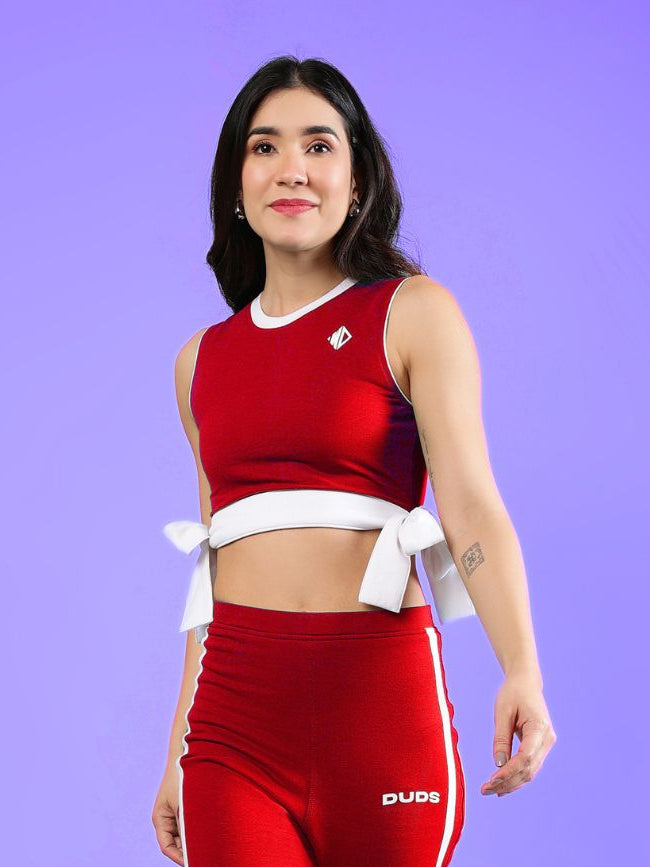 WOMENS FITTONIA COOL CROP TOP RED worn by a woman, showcasing its stylish design against a vibrant purple background.