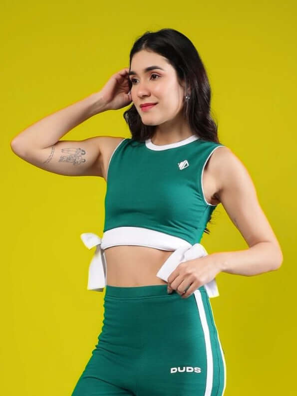 Woman modeling a teal green crop top with white accents against a yellow background, showcasing fashion and style.