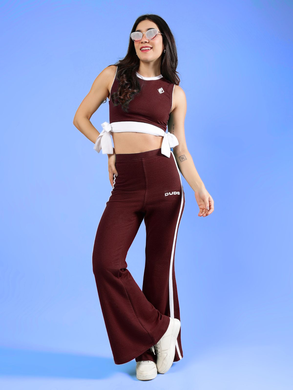 WOMENS FITTONIA COOL WIDE FLARE JOGGERS MAROON shown on a model posing with a blue background and stylish sunglasses.