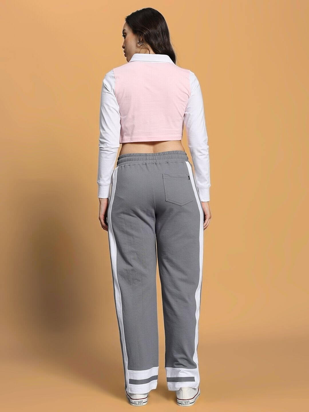 Model wearing WOMEN'S FLORA CO-ORD SET PINK GREY, showcasing back view with pink top and grey pants against a beige background.