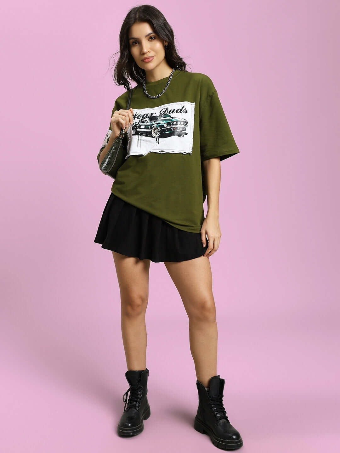 Woman wearing an oversized olive green Ford Mustang t-shirt with black skirt and boots, styled with a casual chic look.