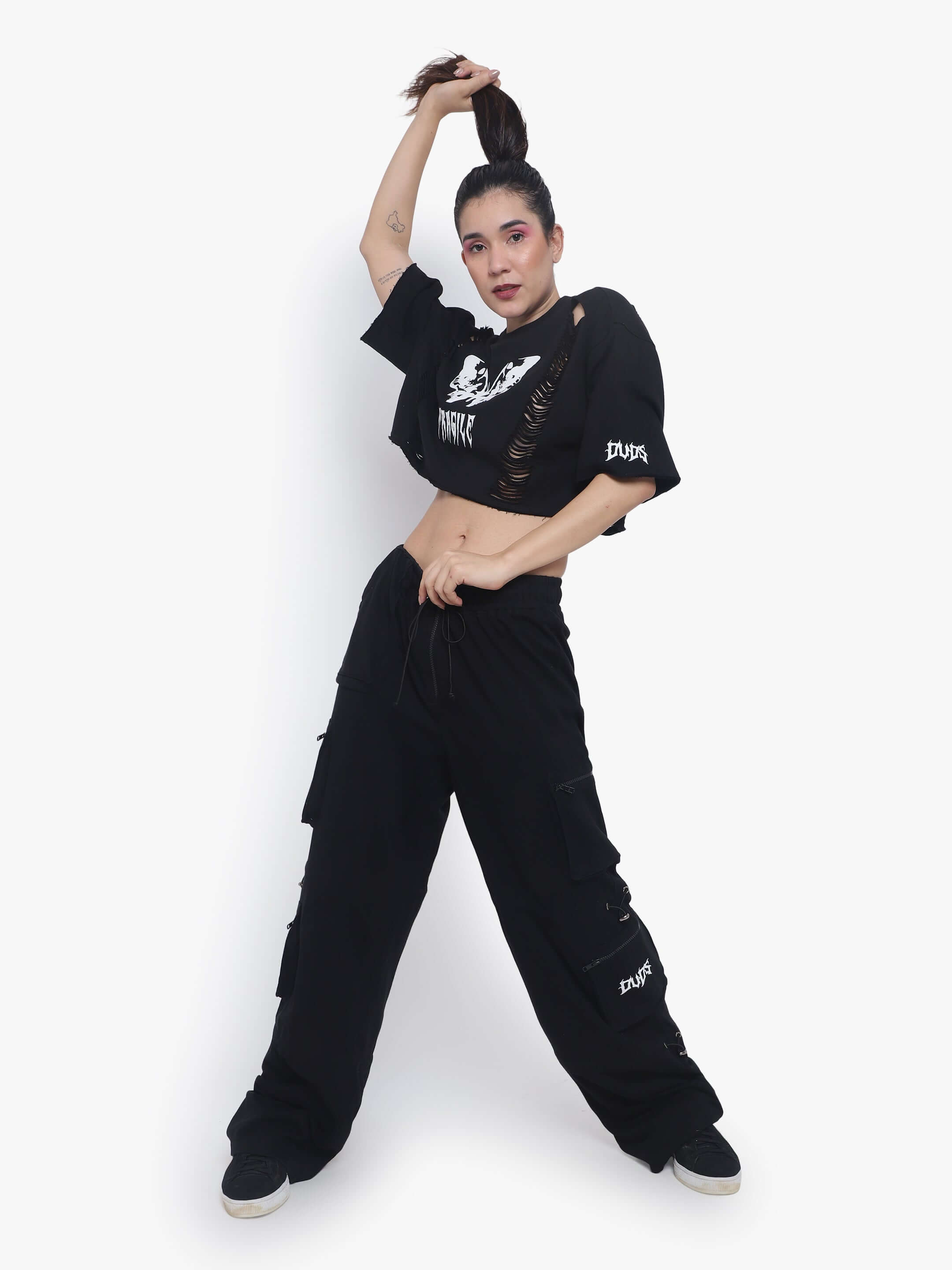 Model wearing a black oversized cropped t-shirt paired with black cargo pants, posing with arm raised, showcasing streetwear fashion.