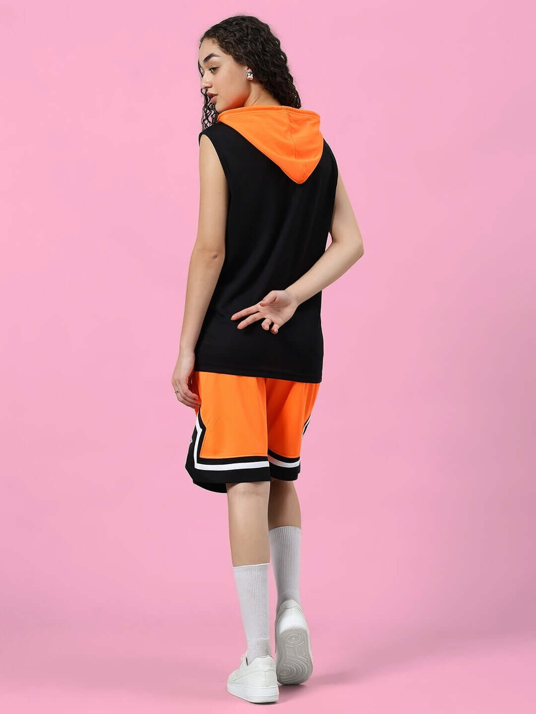 Woman modeling WOMEN'S FRANKY GYM CO-ORD SET ORANGE BLACK, sporty polyester with orange shorts and black top, back view.