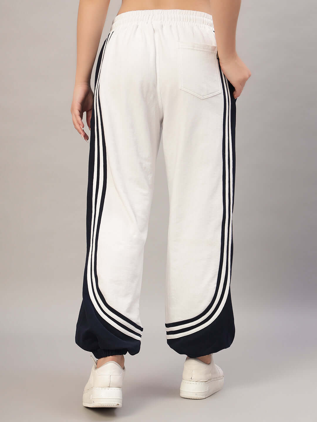 Women wearing white-navy contrast joggers with stripe details, showcasing back view, styled with white sneakers for sporty look.