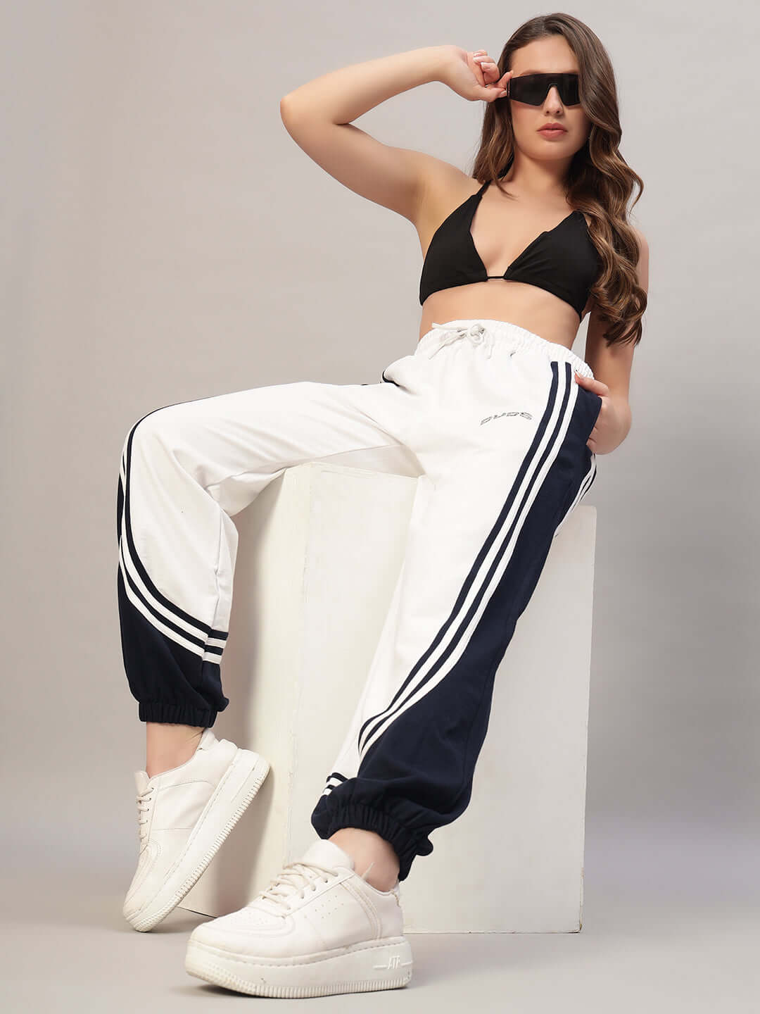 Fashion model wearing women's white and navy contrast joggers, styled with a black top and white sneakers, showcasing DUDS custom fit option.