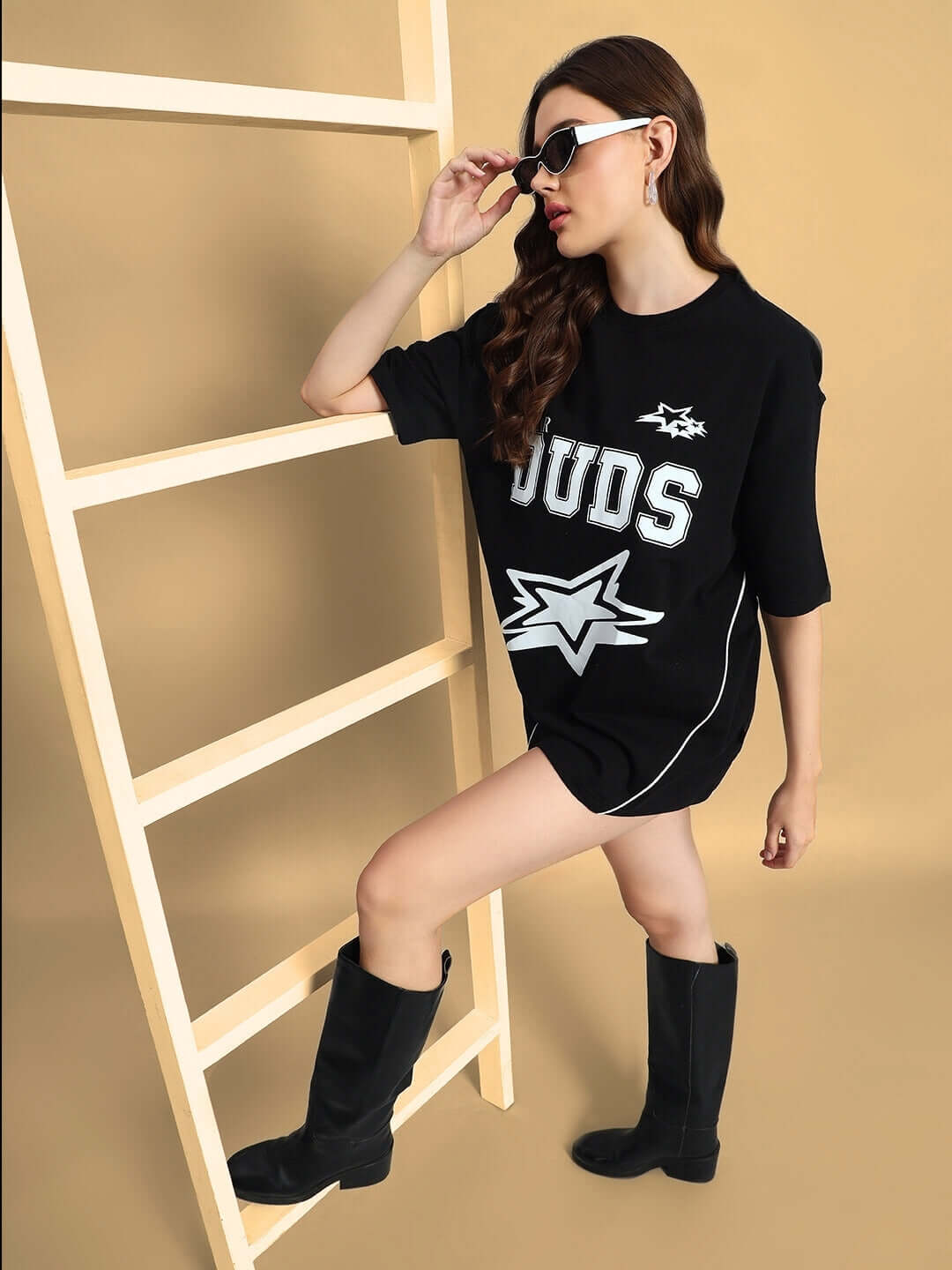 Model wearing DUDS Women's Galaxy Oversized Black T-Shirt with stylish graphics, posing indoors with ladder, highlighting casual chic style.