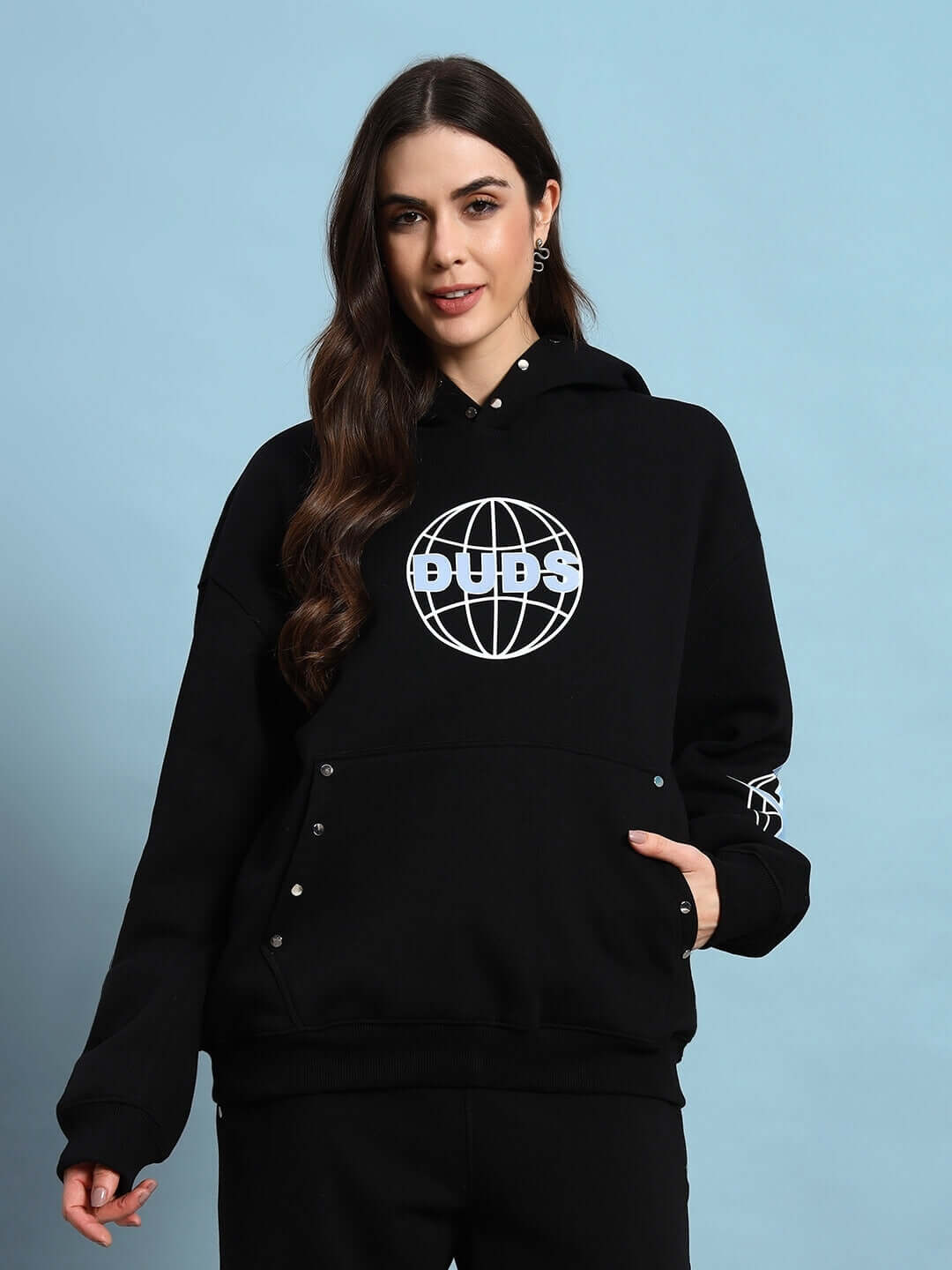 Woman wearing the WOMEN GLOBAL FLEECE HOODIE BLACK with globe graphic, showcasing casual streetwear style.