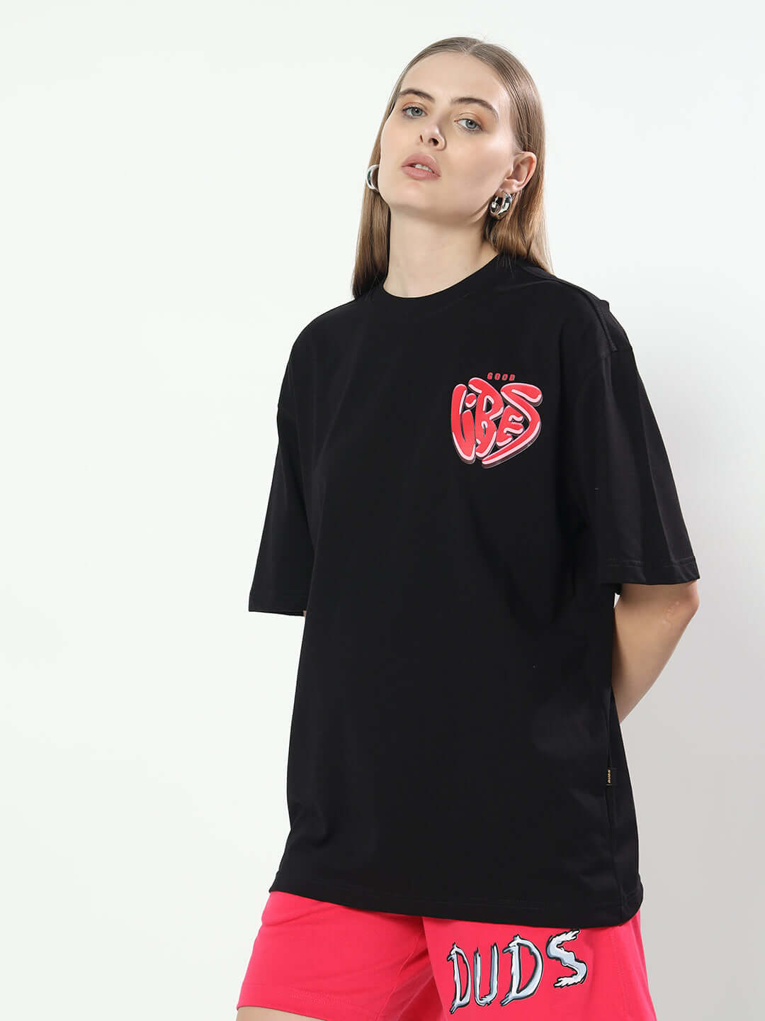 Woman wearing black oversized t-shirt with 'Good Vibes' graphic, styled with red shorts. Ideal for relaxed, trendy fashion.
