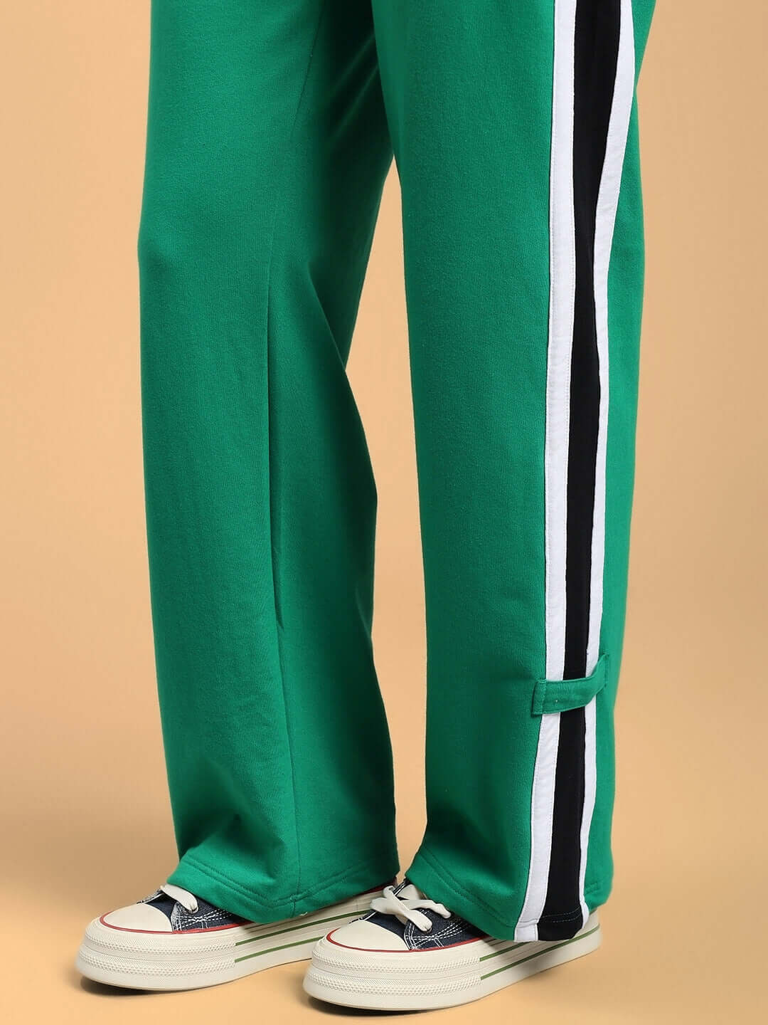 Green women's joggers with side stripes, featuring a relaxed fit, styled with sneakers on a beige background.