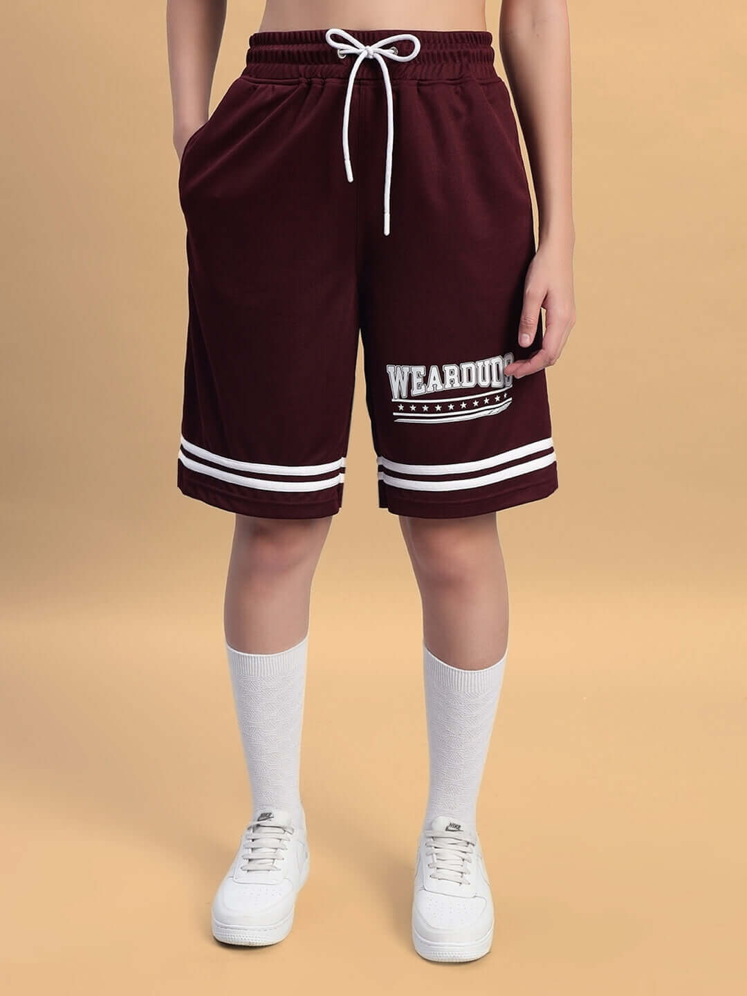 Model wearing WOMEN'S GROOVY COLORBLOCK CO-ORD SET WINE by WEAR DUDS, showcasing wine-colored shorts with white stripes and sneakers.