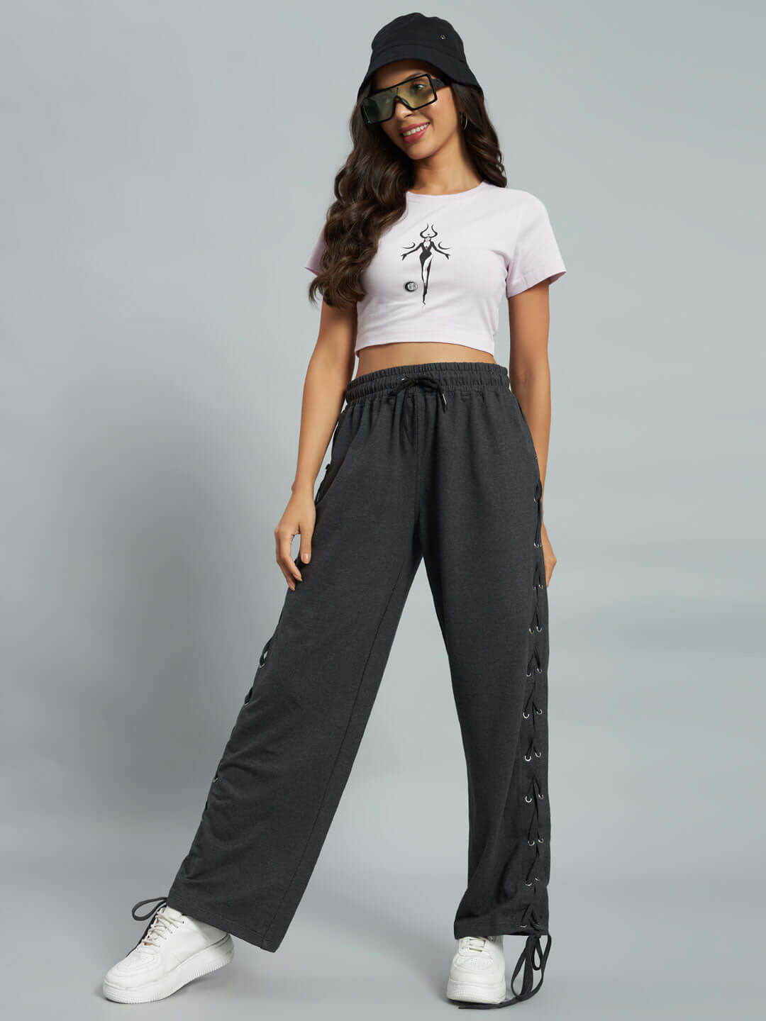 Model wearing grey women's relaxed fit joggers with a black side tie detail, paired with a white crop top and sneakers.