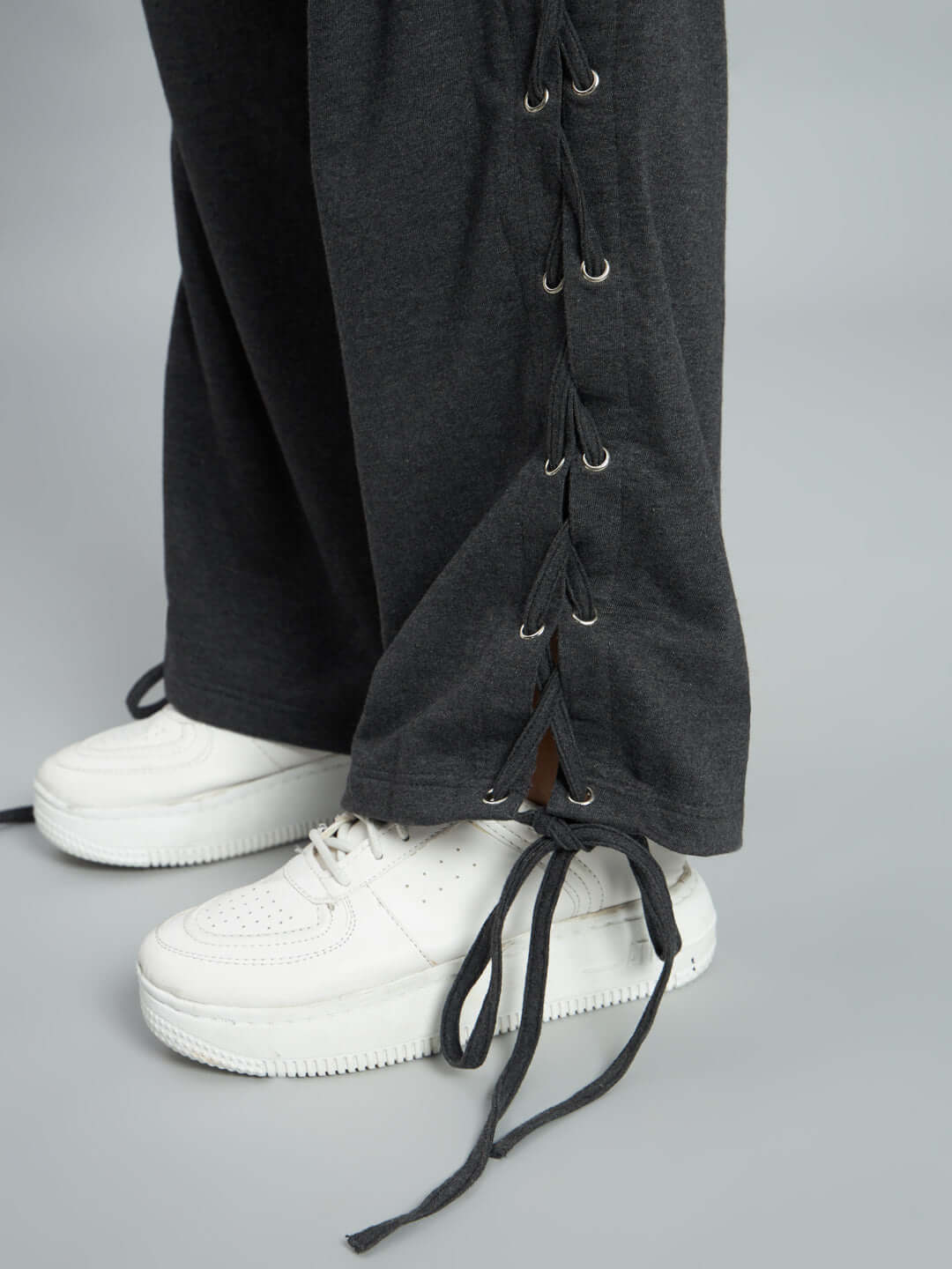 Close-up of grey women's relaxed fit joggers with lace-up detail, styled with white sneakers on a light grey background.