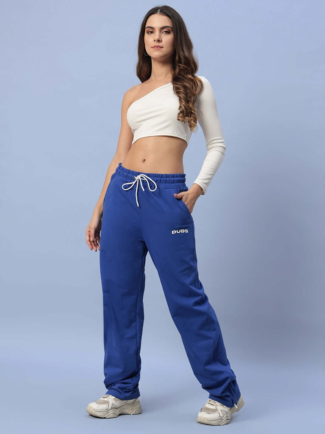 Model wearing women's royal blue joggers with side slits by DUDS, paired with a white off-shoulder top; made-to-order fashion piece.