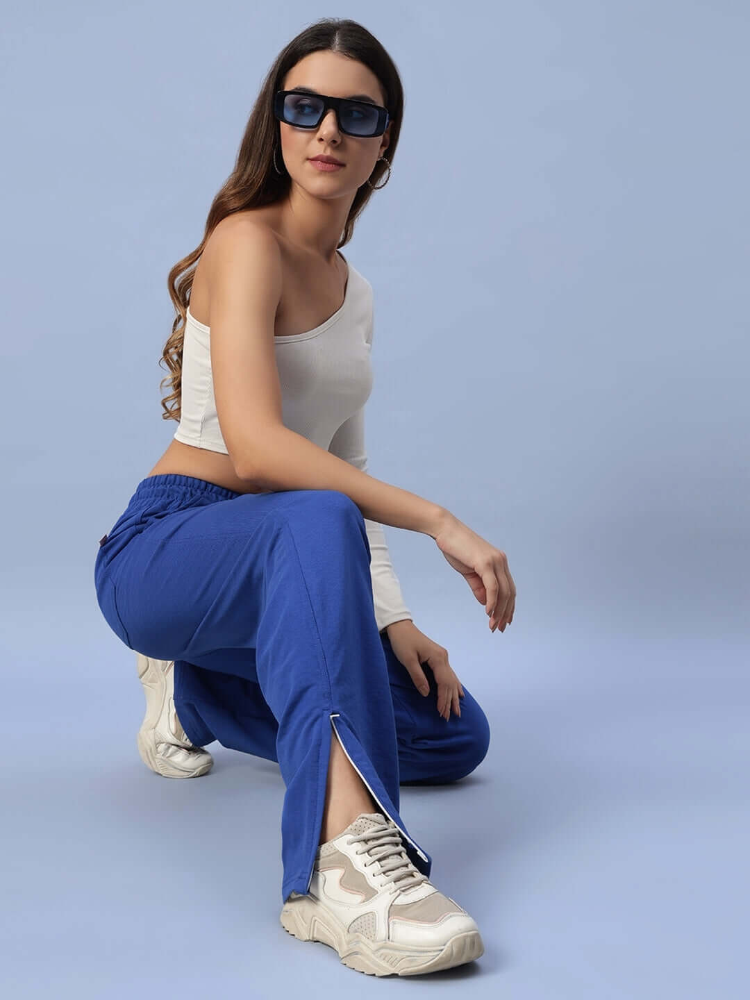 Woman wearing Hershey side slit joggers in royal blue, paired with white top and sneakers, posing stylishly against a blue backdrop.