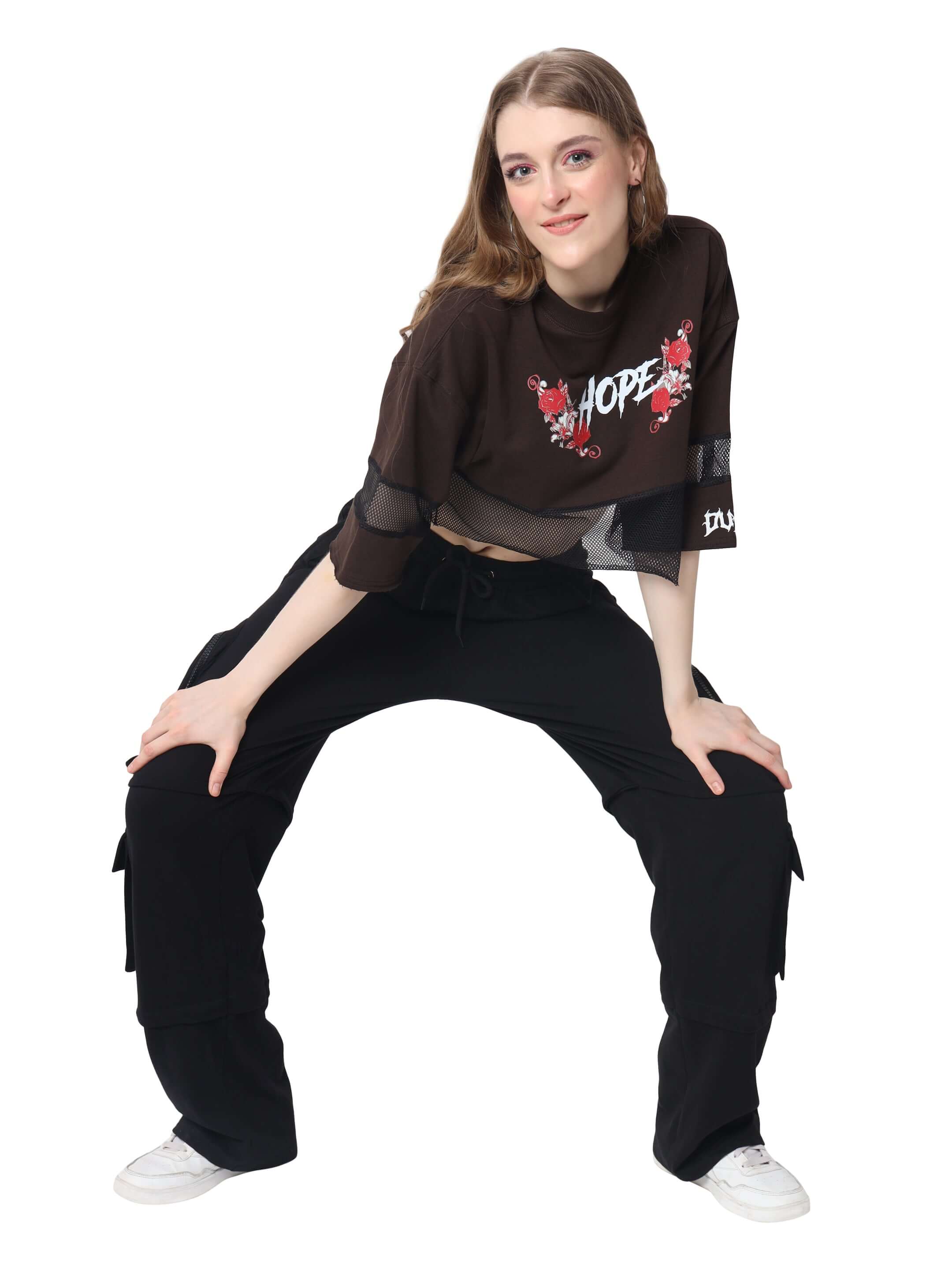 Woman wearing a brown oversized cropped t-shirt with 'HOPE' design, paired with black pants and sneakers. Fashionable casual wear.