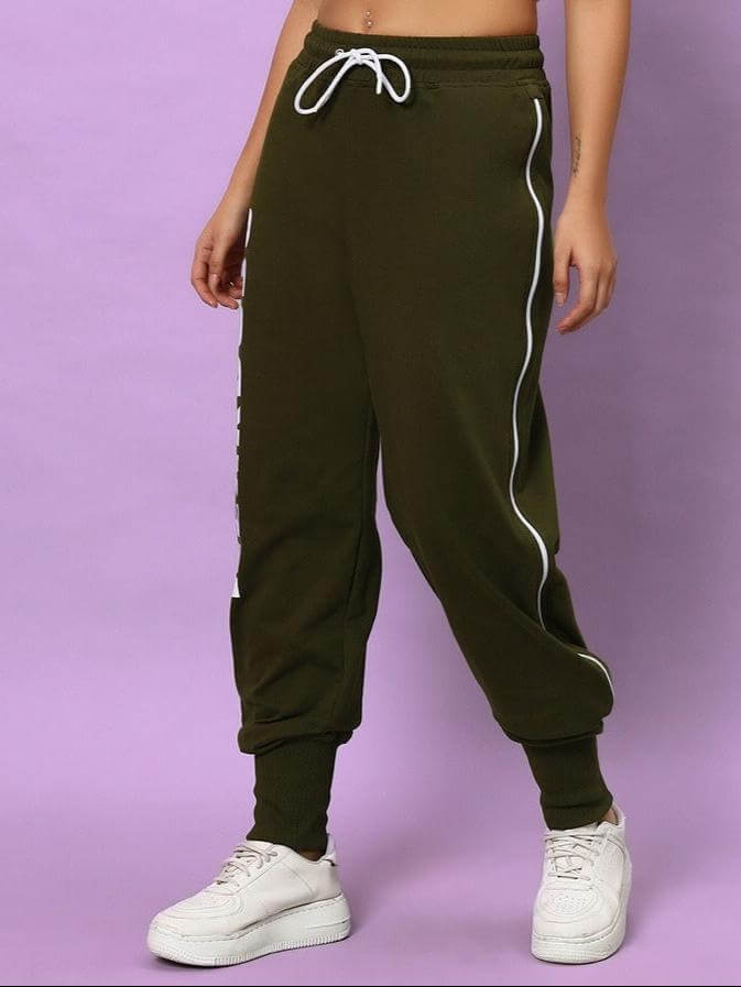 Model wearing Women's Hunter Joggers in olive green with drawstring, featuring a relaxed fit and white sneakers, standing against a purple backdrop.