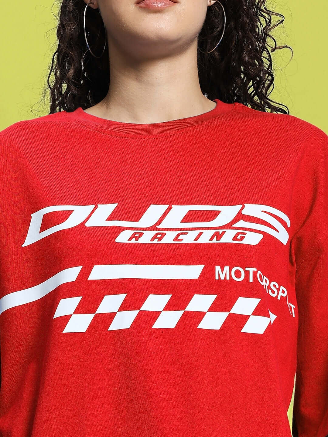 Woman wearing red oversized t-shirt with racing print, made from premium cotton blend fabric, standing against a green background.