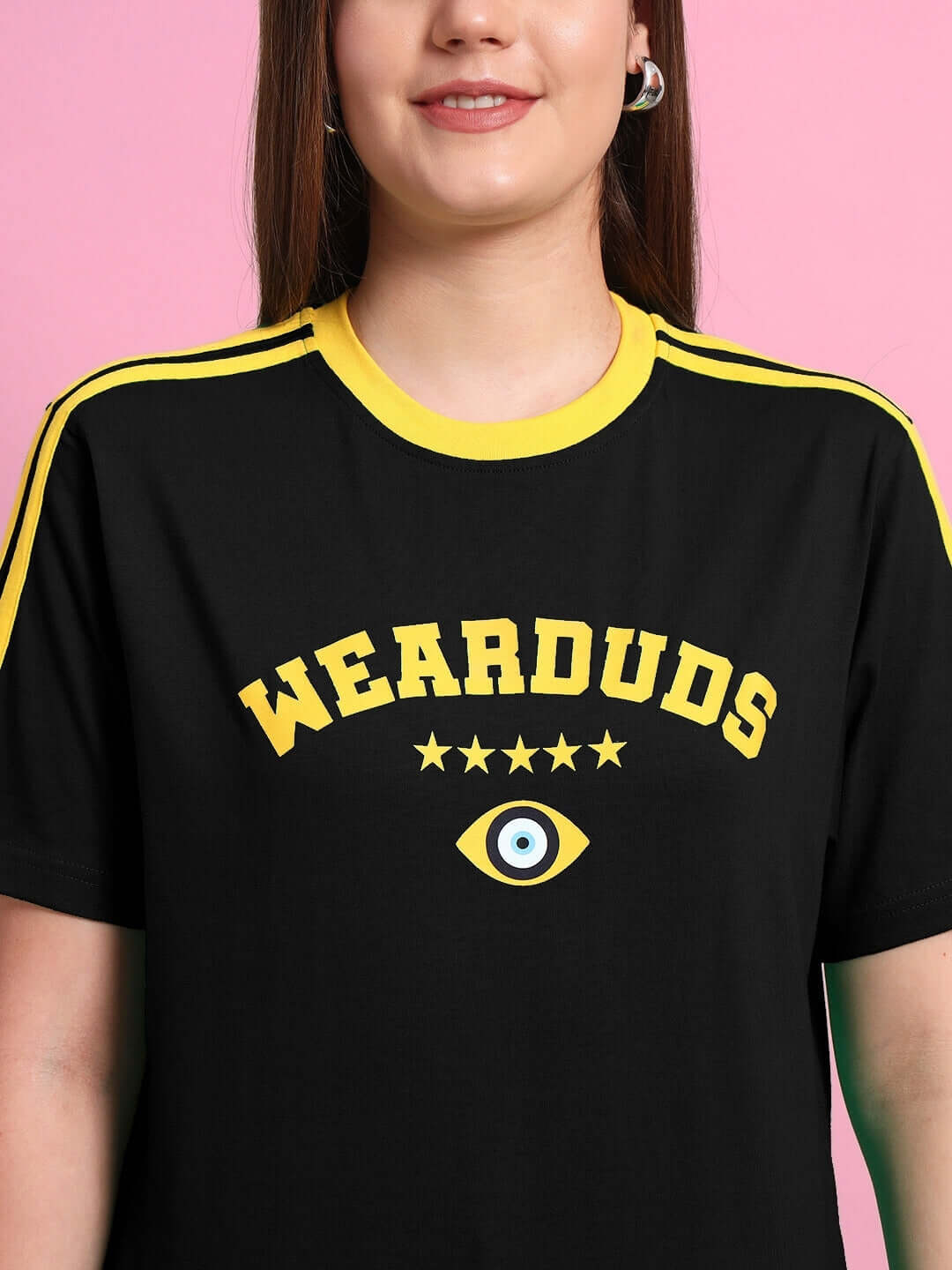 Woman wearing black t-shirt with yellow accents and 'WEARDUDS' logo, pink background.