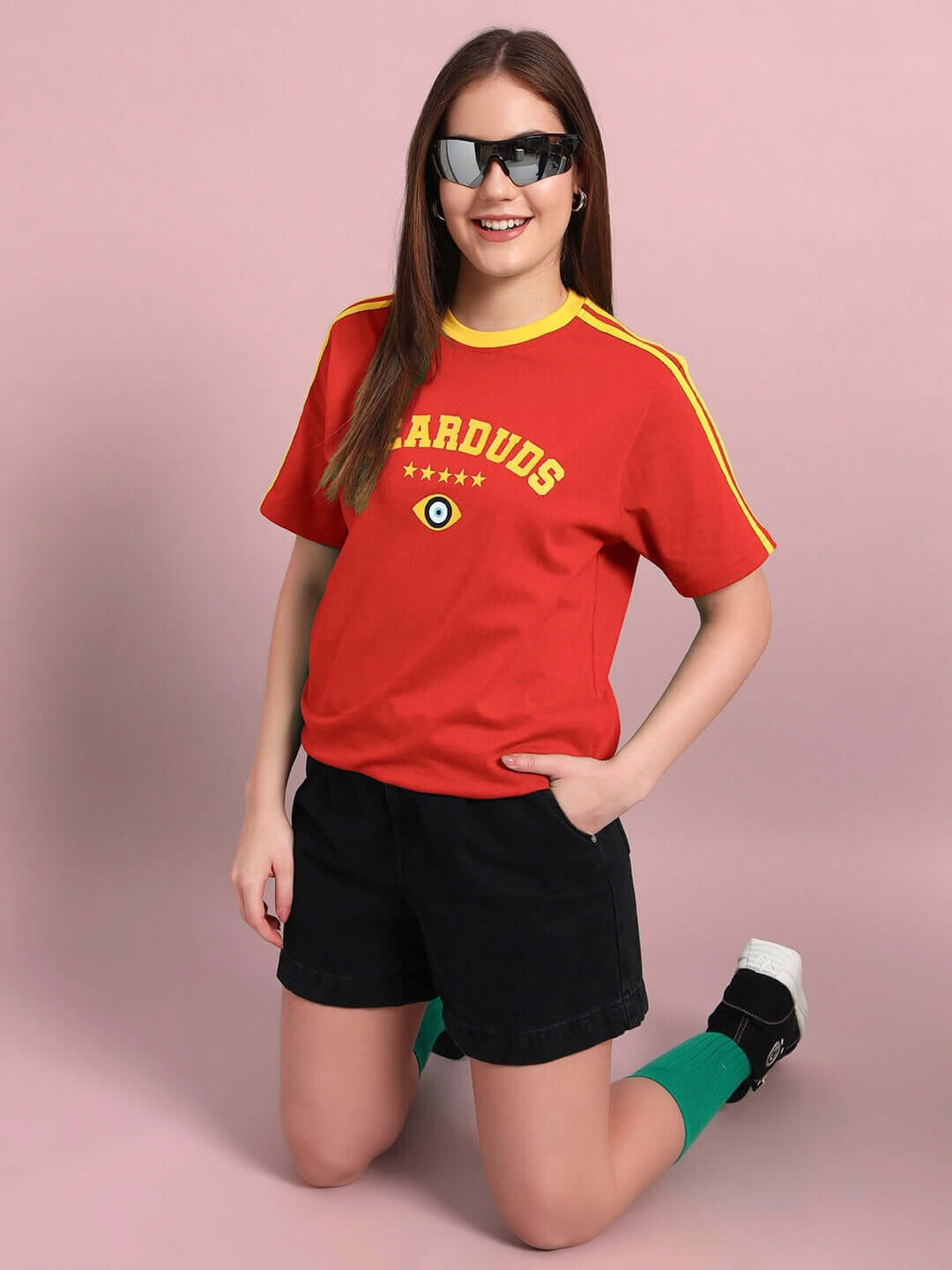 Woman wearing a red women's Irish regular fit t-shirt with yellow stripes on the sleeves, paired with black shorts and green socks. Fashionable and casual look.