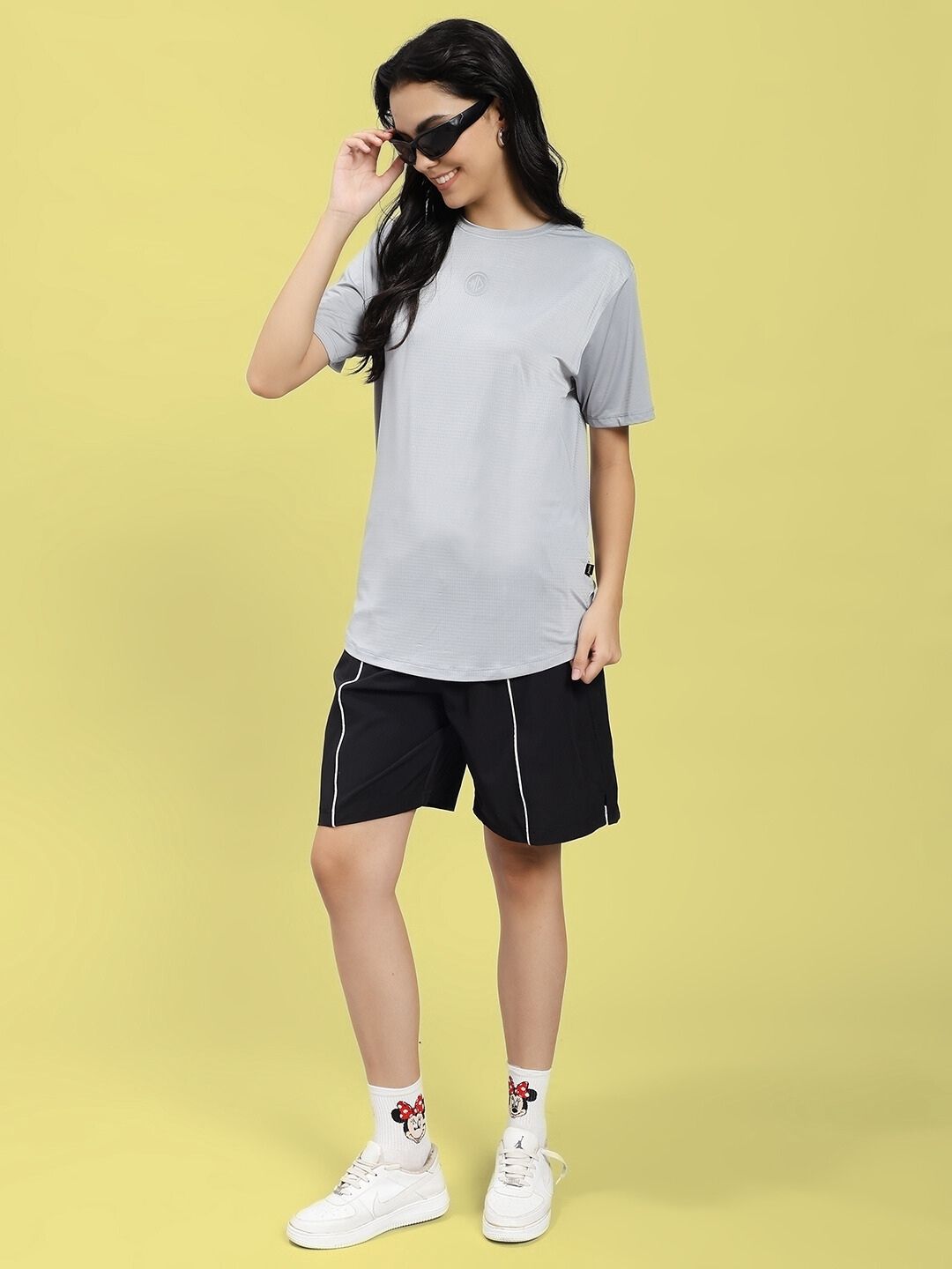 Woman wearing WOMEN JET RUN REGULAR FIT T-SHIRT GREY standing against yellow background.