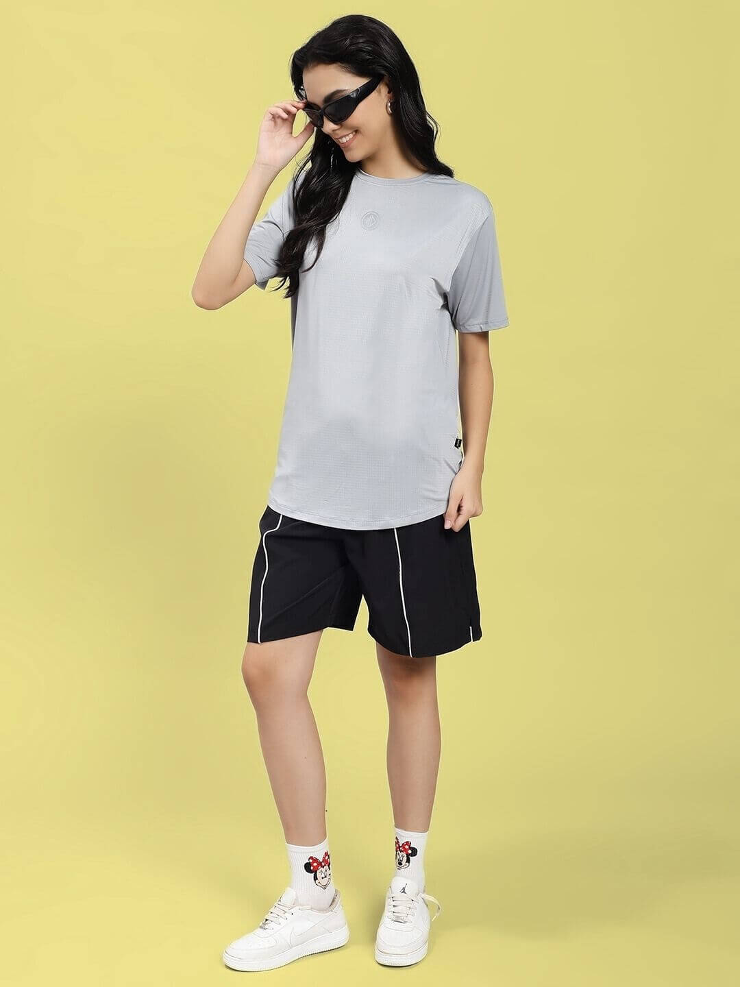 Woman wearing WOMEN JET RUN REGULAR FIT T-SHIRT GREY with shorts and sunglasses, showcasing a casual look.
