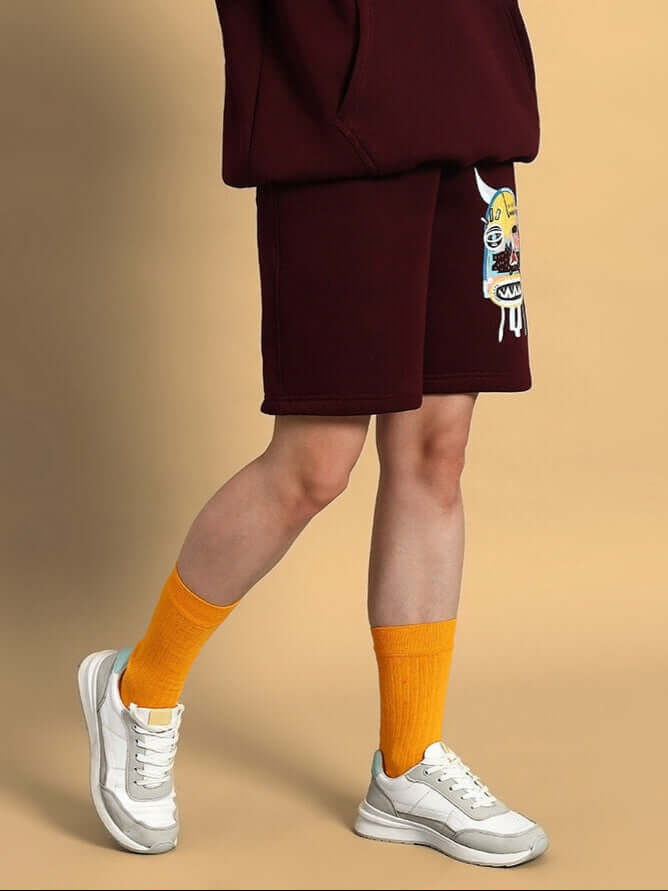 Person wearing Women Jumbled Fleece Shorts Wine with graphic and yellow socks, showcasing stylish streetwear and comfort.