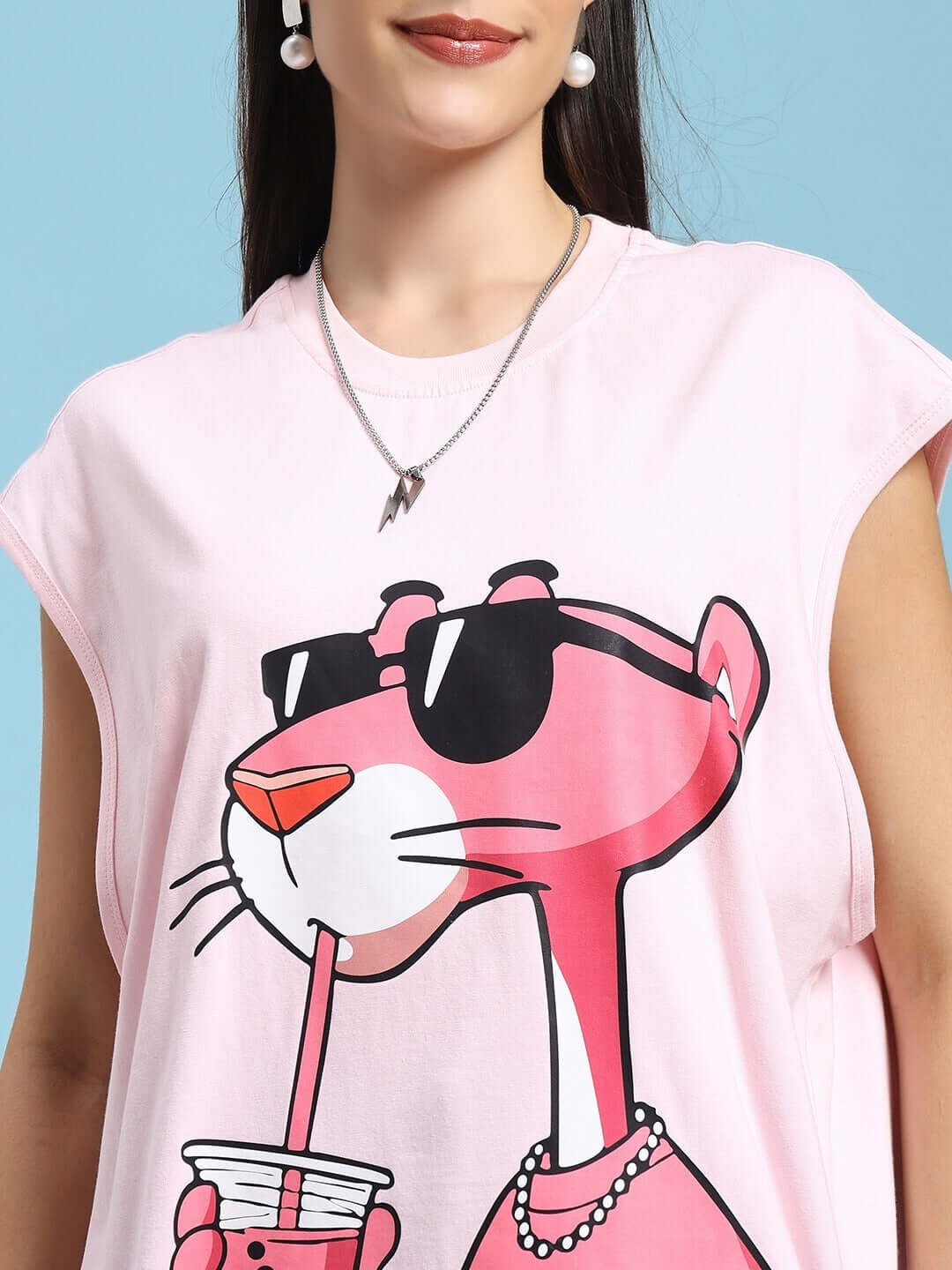 Woman wearing a pink t-shirt with a Pink Panther print, featuring sunglasses and a drink. Ideal for casual wear.