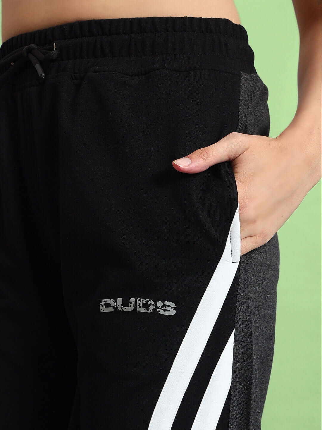 Close-up of women's black grey Korean baggy joggers with a hand in pocket, featuring sporty white stripes and DUDS logo.