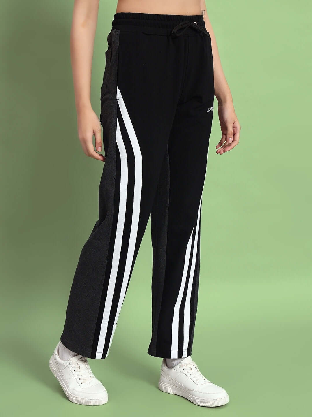 Woman wearing black and grey skater Korean baggy joggers with white stripes, styled with white sneakers, against a green background.