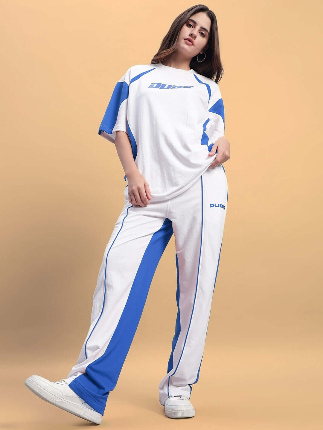 Model wearing Women's Lagoon Relaxed Fit Joggers in white and blue, showcasing a sporty, comfortable look by DUDS on a beige background.