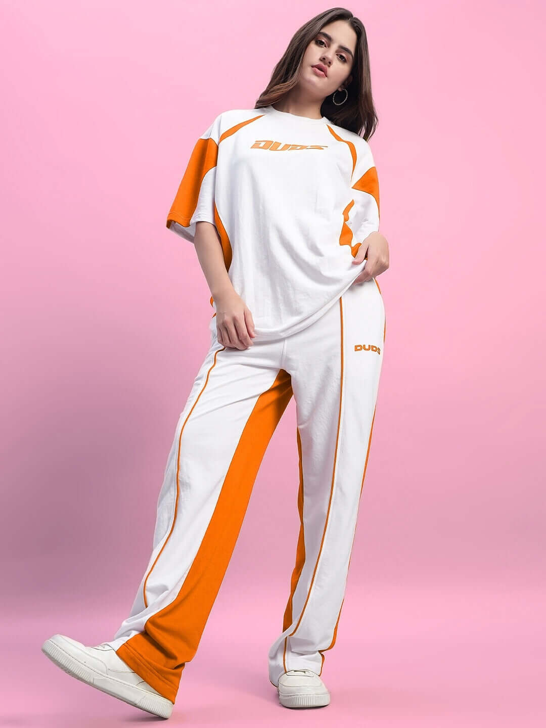 Model wearing white and orange Women's Lagoon Relaxed Fit Joggers, standing against a pink background, showcasing comfortable casual wear.