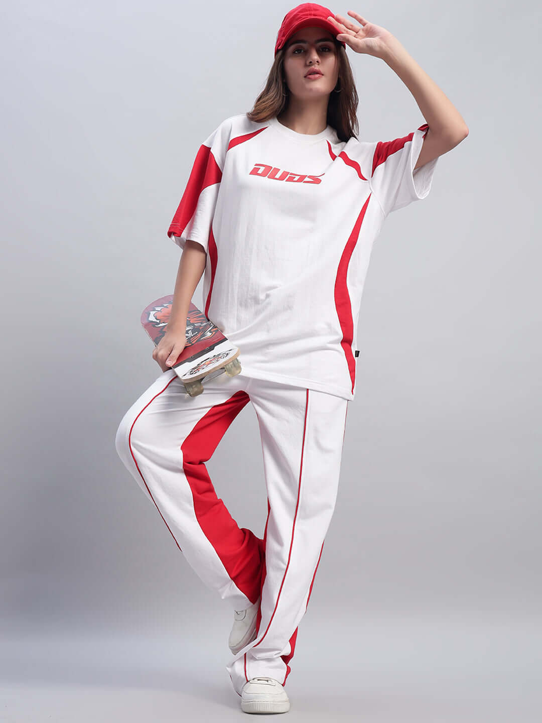 Woman wearing white and red relaxed fit joggers and t-shirt, holding a skateboard, showcasing sporty style fashion.