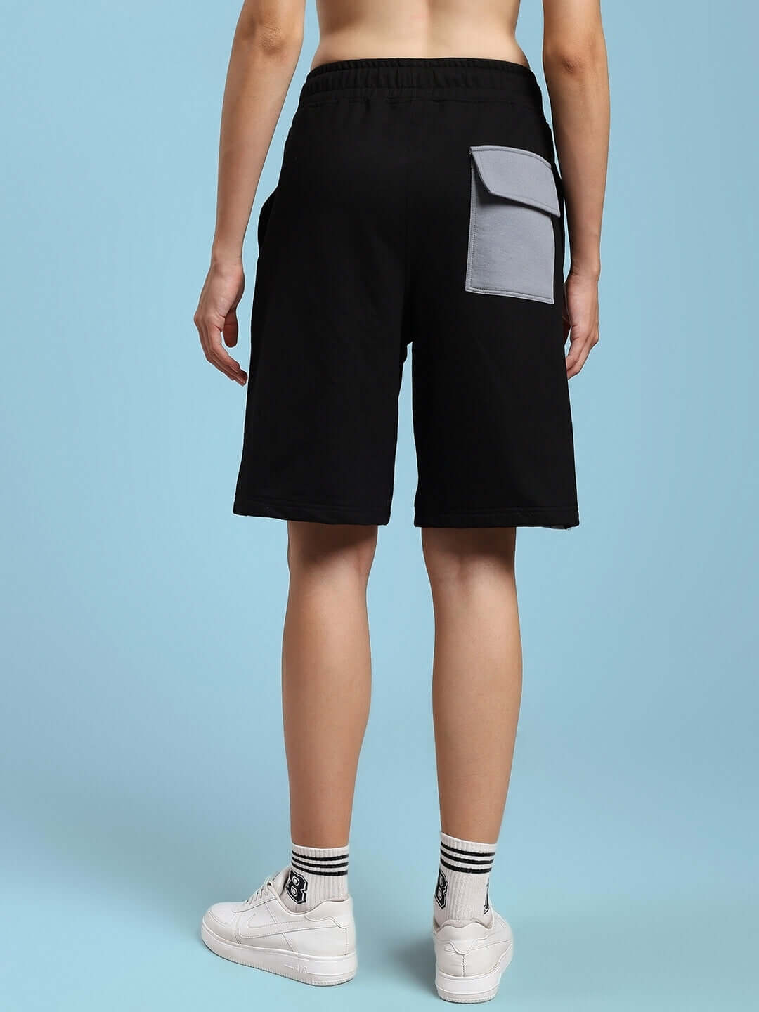 Model wearing women's Lewin Chino regular fit shorts in black-grey, featuring a pocket detail, viewed from the back on a blue background.