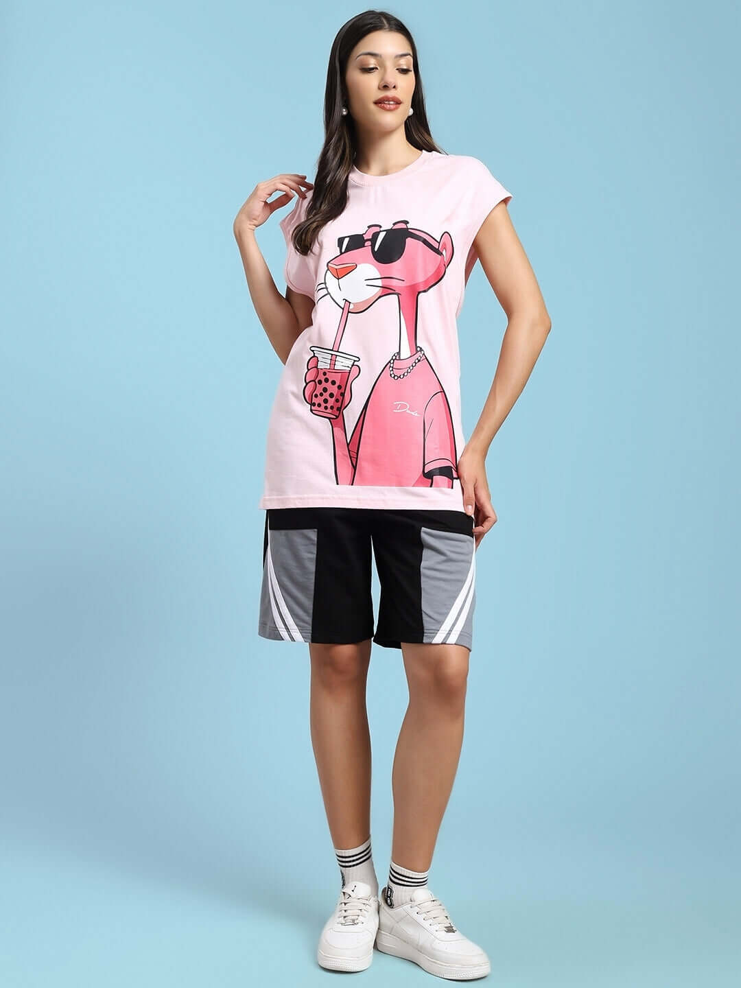 Woman wearing pink graphic t-shirt and black-grey sports shorts against blue background