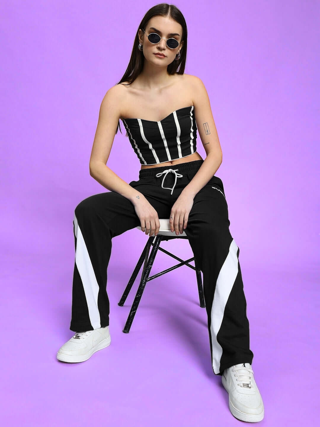 Model wearing WOMEN'S LIVIANA COOL CO-ORD SET BLACK, seated on a chair against purple background, by WEAR DUDS.