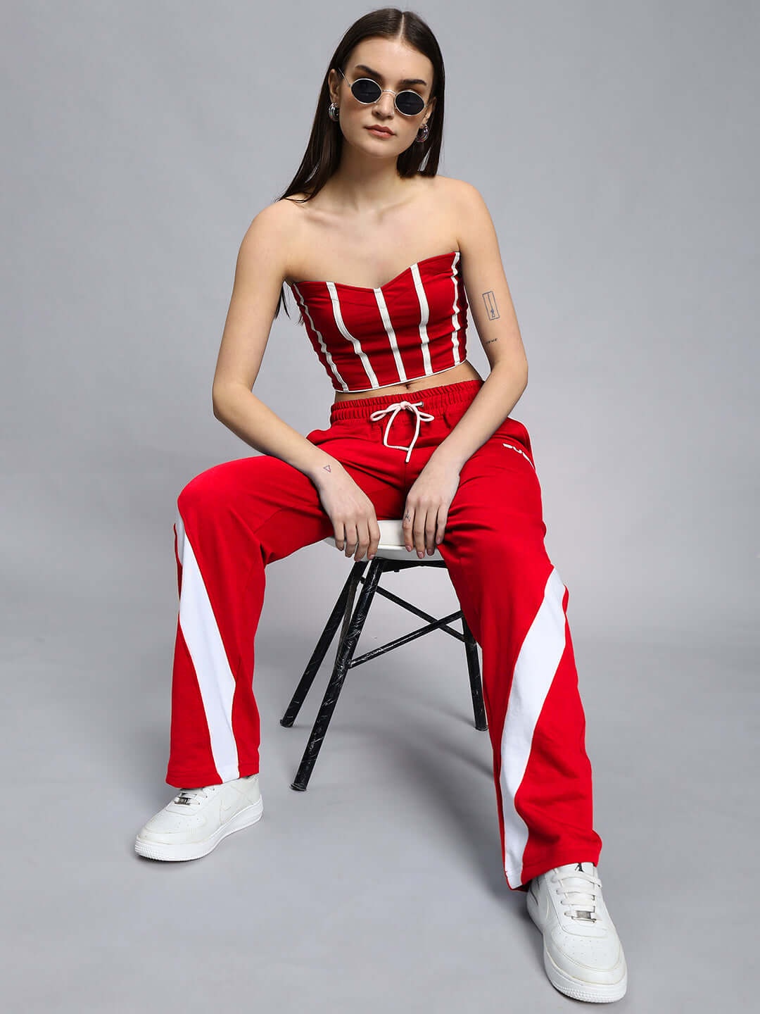 Fashion model wearing WOMEN'S LIVIANA COOL CO-ORD SET RED, seated on chair, showcasing bold red and white streetwear style.