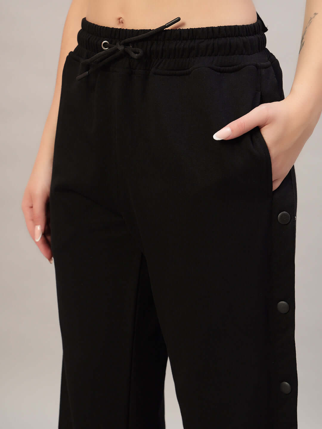 Close-up of black women's Mambo joggers with drawstring waist and side buttons, modeled by a person with hands in pockets.